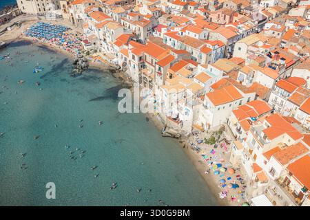 Vue aérienne des plages baignées de soleil rencontrant les toits en terre cuite vibrante des bâtiments historiques, un contraste saisissant avec la mer turquoise, Cefalù, Sicile, Italie. Banque D'Images