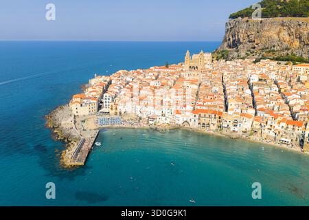 Vue aérienne de la lumière dorée du soleil baignant les toits en terre cuite de Cefalù, contrastant avec les eaux turquoises et l'imposante Rocca di Cefalù, Cefalù, Sicile, Italie. Banque D'Images