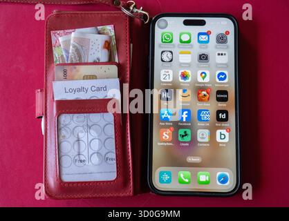 iphone 14 pro max montrant l'écran d'accueil avec des applications, protégé dans un étui pliant en cuir rouge qui a des fentes pour les cartes de crédit / espèces, l'argent et les reçus. Banque D'Images