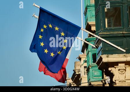 Drapeau de Malte et drapeau de l'Union européenne battent le paysage urbain historique dans un éclairage chaud Banque D'Images