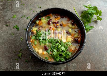 Soupe de haricots rouges avec pommes de terre, tomates, paprika, carotte et bacon sur une table en pierre. Vue de dessus. Copier l'espace. Banque D'Images