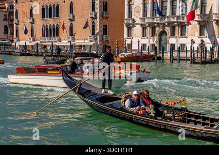 Les taxis privés passent derrière une gondole prenant deux personnes pour une promenade en gondole sur un Grand canal animé à Venise, en Italie Banque D'Images