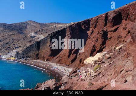 Santorin, GR - 4 septembre 2025 : la célèbre plage rouge de Santorin, montrant des roches volcaniques rouge vif et du sable à côté de la mer Égée bleu clair Banque D'Images