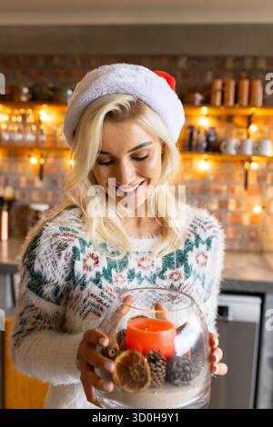 Femme tenant la pièce maîtresse de vacances dans la cuisine portant un pull de Noël et chapeau de Père Noël Banque D'Images