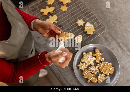 Les mains coulent le glaçage sur le biscuit étoile des fêtes avec le sac à passepoil sur le comptoir à côté du support de refroidissement Banque D'Images