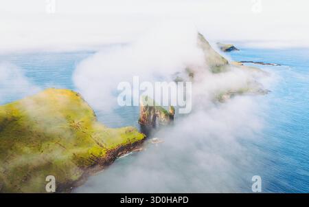 Vue aérienne des falaises déchiquetées de Drangarnir perçant à travers les brumes tourbillonnantes au-dessus de la mer bleue profonde, Drangarnir, îles Féroé. Banque D'Images