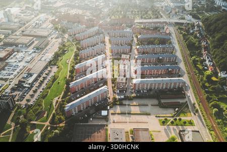 Vue aérienne de rangées soignées de bâtiments au toit rouge contrastent avec les arbres verdoyants, créant un mélange harmonieux de paysages urbains et naturels, Vejle, Danemark. Banque D'Images