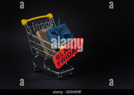 Panier miniature plein de cadeaux pour le vendredi noir avec étiquette rouge sur fond noir Banque D'Images