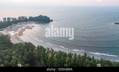 C'est une belle image de coucher de soleil sur l'océan, avec une petite île ou masse terrestre au premier plan. Les teintes dorées du soleil se fondent harmonieusement en t Banque D'Images