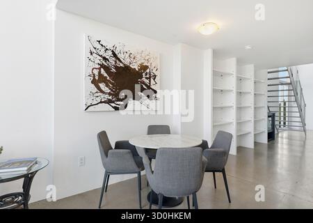 Peinture abstraite blanche et noire accrochée au mur au-dessus d'une table à manger. La table est équipée de quatre chaises et d'une table en verre. La chambre dispose d'un a moderne Banque D'Images