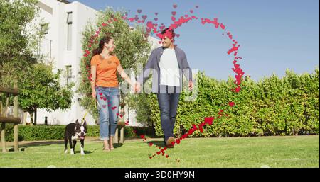 Couple marchant tenant les mains sur la pelouse verte dans la cour, avec chien Boston Terrier et des coeurs rouges Banque D'Images