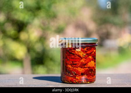 Tomate rouge séchée au soleil avec ail, romarin, huile d'olive et épices dans un bocal en verre sur une table en bois. Style rustique, gros plan Banque D'Images