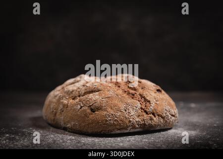 Pain complet rond de levain épeautre avec noix sur ardoise foncée, vue d'angle latérale montrant la croûte et la texture, composition centrée. Banque D'Images