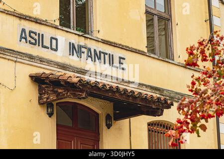 Façade de bâtiment historique à Monteu da po, Italie, avec un panneau altéré lisant Asilo infantile. Les murs en plâtre jaune, porte en bois Banque D'Images