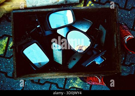 Pile de vieux miroirs de voiture empilés dans une boîte en bois à un marché aux puces, présentés comme des pièces métalliques usées avec une sensation vintage rustique. Banque D'Images