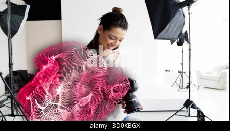 Examinant femme photographe examinant des images sur appareil photo reflex numérique en studio, avec superposition d'onde rose Banque D'Images