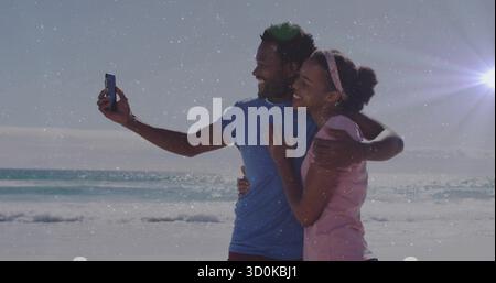 Prise selfie couple penché l'un dans l'autre sur la plage de sable au coucher du soleil, avec smartphone Banque D'Images