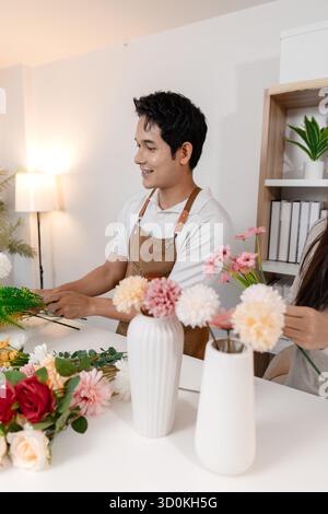 Un jeune couple arrangeant des fleurs colorées ensemble dans un cadre de maison confortable. L'homme, portant un tablier, aide la femme à créer un beau bouquet, shar Banque D'Images
