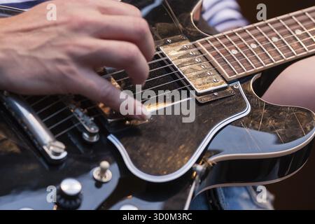 Gros plan des mains d'un homme pincant les cordes sur une guitare électrique décorative en bois avec l'accent sur le pick-up et les cordes Banque D'Images