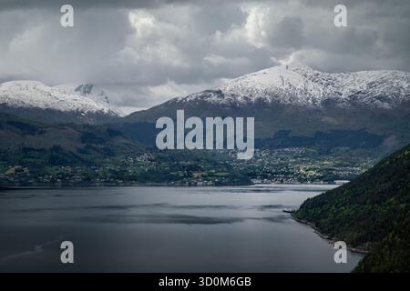 Des montagnes enneigées et des nuages entourent une ville sereine près du fjord norvégien. Banque D'Images