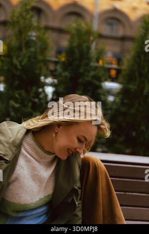 Femme heureuse regardant vers le bas et souriant tout en étant assise sur un banc de parc Banque D'Images