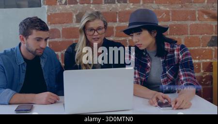 Collaboration de collègues examinant des idées de projet dans un bureau mural en briques, avec ordinateur portable et smartphones Banque D'Images