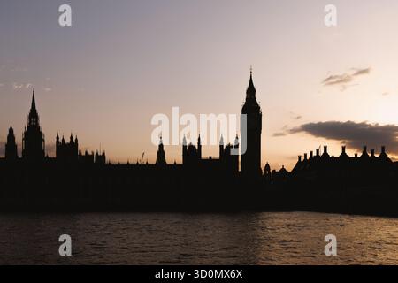 Silhouette des chambres du Parlement et de la tour Elizabeth de l'autre côté de la Tamise au crépuscule. Les tons chauds du ciel se reflètent sur l'eau avec une soirée calme Mo Banque D'Images