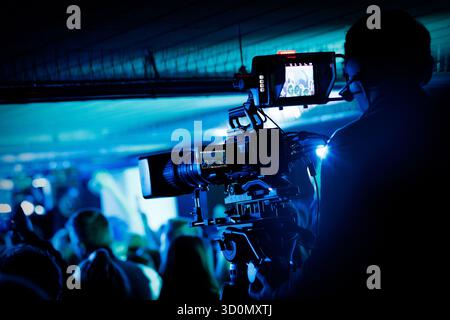 Vue rapprochée du cameraman exploitant la caméra vidéo professionnelle pendant le concert en direct dans un éclairage bleu. Banque D'Images