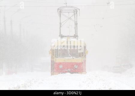 Vieux tramway rouge et jaune conduisant à travers une tempête de neige intense dans la ville, vue de face Banque D'Images