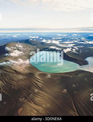 Vue aérienne d'un lac turquoise niché dans un cratère volcanique, la terre sombre et texturée contraste avec l'eau vibrante, Skyggnisvatn, Rangárþing ytra, Islande. Banque D'Images