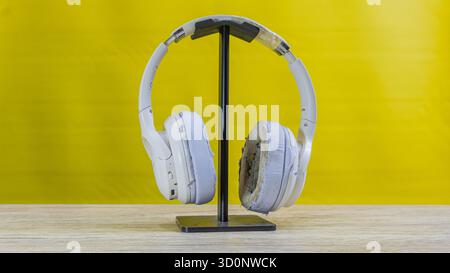 Casque blanc avec des fissures visibles et des dommages d'écaillage placé sur le support noir sur la base en bois, isolé sur fond jaune vif, concept de brok Banque D'Images