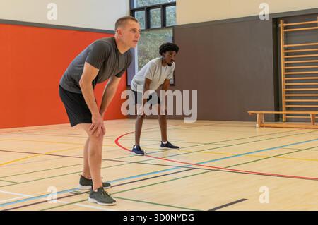 Divers coéquipiers masculins se penchant en avant et se reposant sur le court avec des lignes colorées à l'intérieur du gymnase. Athlètes, travail d'équipe, fitness, gymnase, mouvement, entraînement, force || autorisation du modèle Banque D'Images