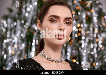 Jeune femme rayonne de beauté dans une tenue festive sur fond de lumières de vacances lumineuses. Banque D'Images