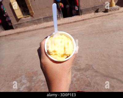 Main tenant une tasse de sorbet jaune vif ou de gelato sur une journée chaude Banque D'Images