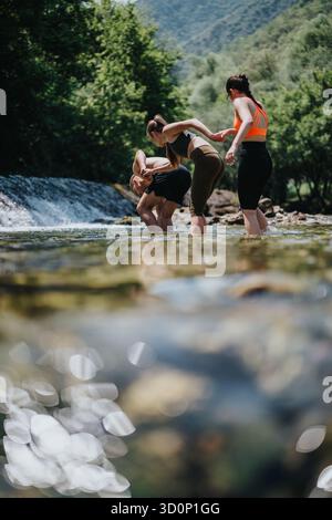 Amis pataugant dans une rivière peu profonde entourée par une forêt luxuriante et la nature Banque D'Images