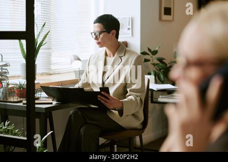 Femme d'âge moyen examinant des documents lorsqu'elle est assise au bureau Banque D'Images