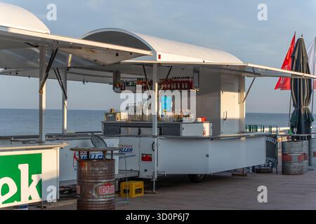 Allemagne Sylt 2 octobre 2025. Vue large d'une remorque de bar mobile au bord de la mer, avec des bouteilles et des verres prêts pour les clients. L'océan et le ciel bleu c Banque D'Images