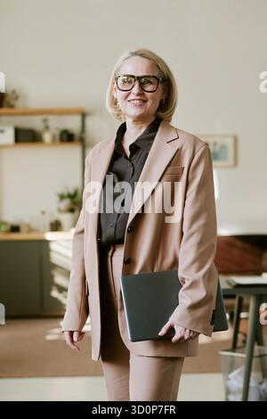 Portrait d'une femme d'âge moyen souriant tout en tenant l'ordinateur portable à l'intérieur Banque D'Images