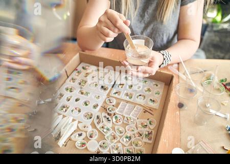 Femme artisan fabriquant des bijoux en résine avec des éléments décoratifs dans un cadre d'atelier. Banque D'Images