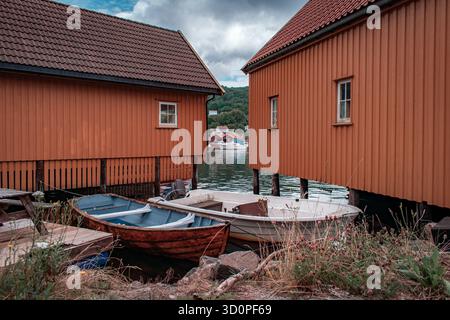 Une rangée de chalets colorés avec des bateaux amarrés à l'intérieur, reflétant sur l'eau calme. Banque D'Images