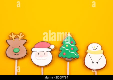 Biscuits glacés sur le thème de Noël en forme de renne, Père Noël, arbre de Noël et bonhomme de neige sur fond jaune Banque D'Images