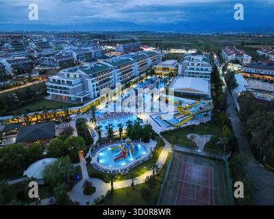 Antalya, Turquie - 13 juillet 2024 : vue aérienne d'un grand hôtel moderne et zone de villégiature avec piscines, toboggans aquatiques et bâtiments illuminés après Banque D'Images