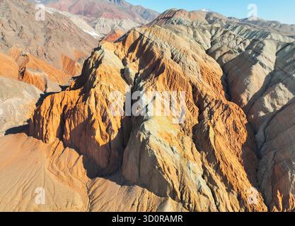 Vue aérienne détaillée montrant les schémas d'érosion complexes et les couleurs orange, rouge et jaune vibrantes d'une pente de montagne abrupte Banque D'Images