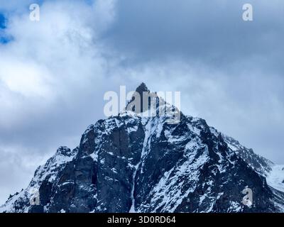 Vue aérienne rapprochée d'un sommet de montagne enneigé et isolé sous un ciel sombre, couvert et bleu foncé Banque D'Images