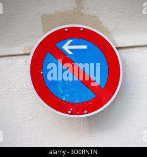 Un panneau de signalisation circulaire avec une bordure rouge, un centre bleu et une barre oblique rouge indiquant « pas de stationnement ». Une flèche blanche pointe vers la gauche. Banque D'Images