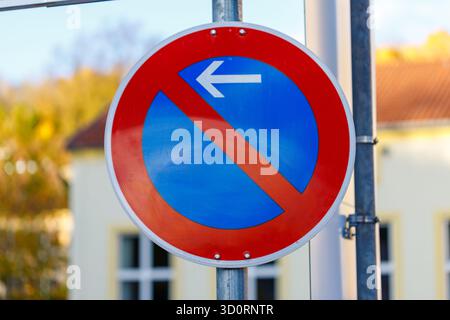 Un panneau circulaire rouge et bleu avec une barre diagonale rouge et une flèche blanche pointant vers la gauche, monté sur un poteau métallique. Banque D'Images