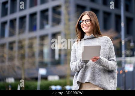 Jeune femme d'affaires occupée heureuse debout dans la ville en utilisant la tablette numérique. Banque D'Images