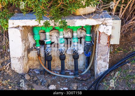 Vue rapprochée des vannes de contrôle d'irrigation et des conduites d'eau vertes dans la boîte en béton sur fond de buissons. Grèce. Kos. Banque D'Images
