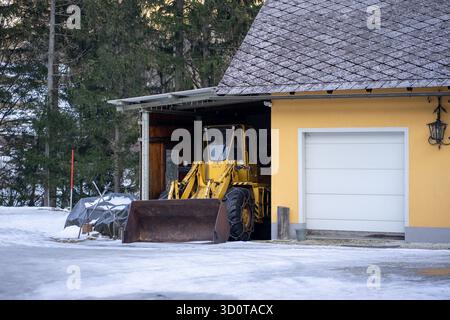 Un tracteur jaune avec des chaînes sur roues est préparé dans le garage pour le déneigement en hiver Banque D'Images