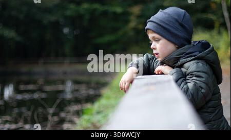 Portrait d'un garçon regardant un lac, fond de forêt floue Banque D'Images